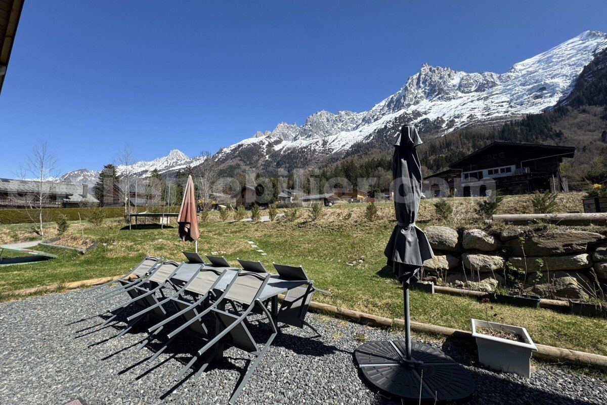A patio with chairs and umbrellas with a mountain in the background and the website immobilier.com