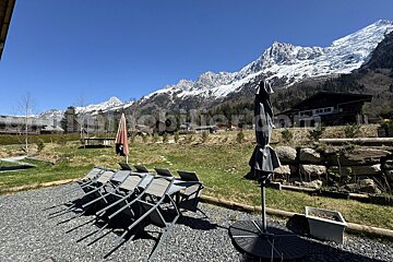 A patio with chairs and umbrellas with a mountain in the background and the website immobilier.com