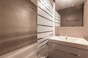 Modern bathroom with a tiled shower/tub, frosted glass screen, white sink vanity, and mirror.
