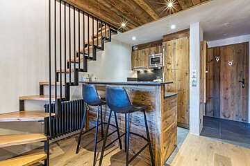 Modern rustic interior featuring a floating wooden staircase, a kitchen bar with two black stools, and warm wood accents.