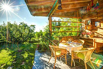 A table and chairs on a porch with the sun shining through the trees