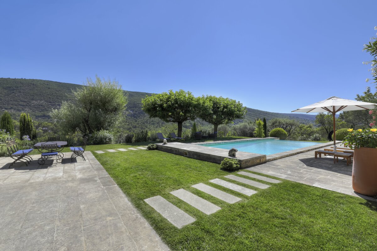 A large swimming pool is surrounded by a lush green lawn