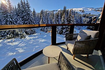A chair and table on a balcony overlooking a snowy forest