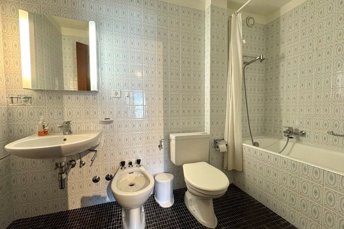 Retro-tiled bathroom with a white sink, mirror, bidet, toilet, and a bathtub with a shower curtain.