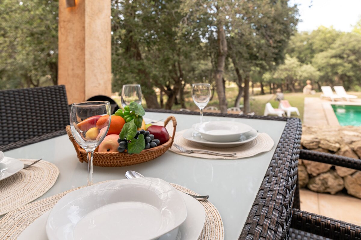 A bowl of fruit sits on a table next to wine glasses