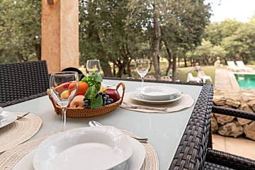 A bowl of fruit sits on a table next to wine glasses