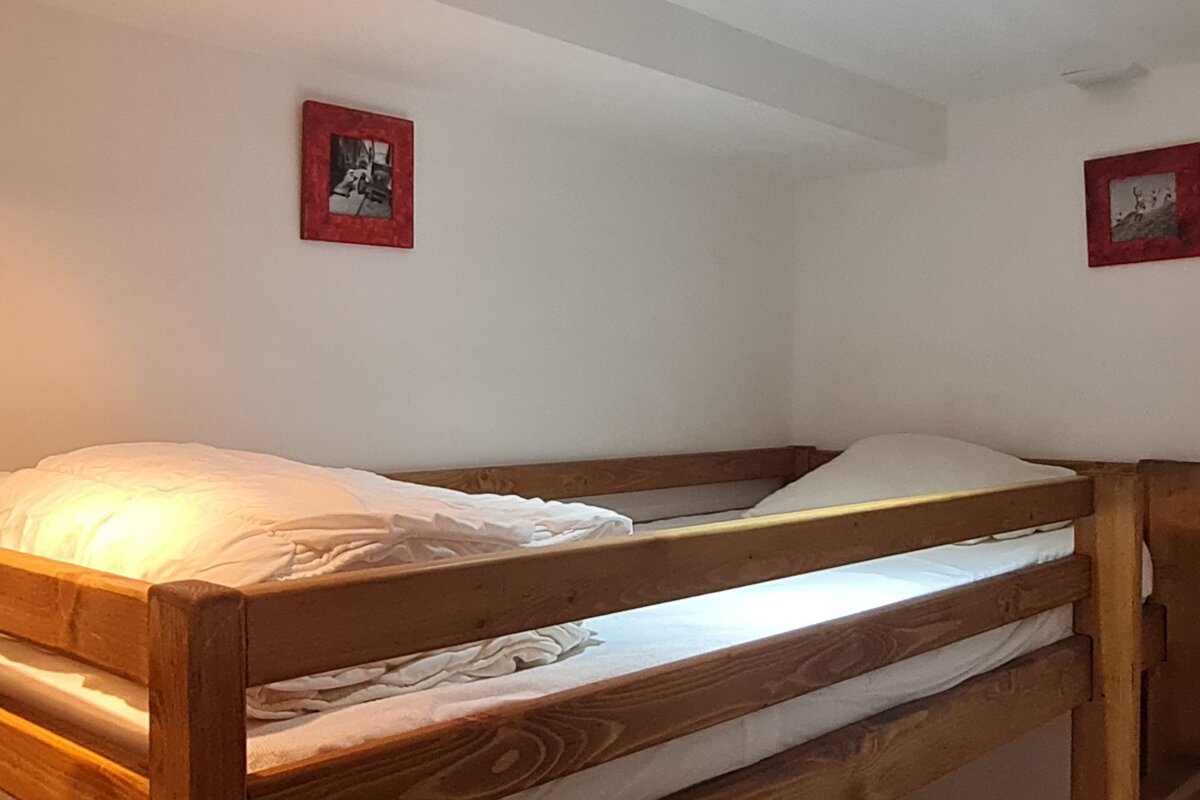 A cozy bunk bed room with wooden frames, white bedding, and white walls featuring two small red-framed pictures.