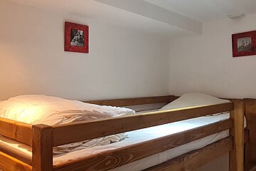 A cozy bunk bed room with wooden frames, white bedding, and white walls featuring two small red-framed pictures.