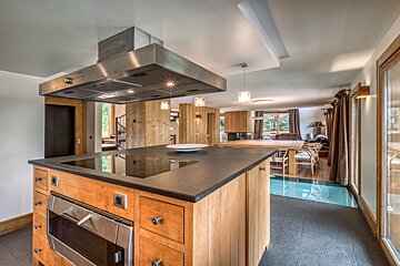 Modern kitchen island with oven, hob & range hood in an open-plan room with wood-paneled walls and a living/dining area.