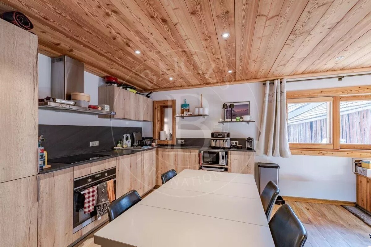 A cozy wooden kitchen featuring a plank ceiling, light wood cabinets, and a white dining table with black chairs.