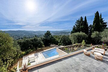 An expansive patio features an infinity pool, outdoor lounge, and panoramic views of lush hills and valleys under a clear sky.