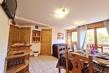 A rustic chalet dining room with a set wooden table for a meal, wooden furniture, and large windows revealing a scenic outdoor view.