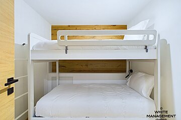 A bunk bed with white sheets and white management written on the bottom