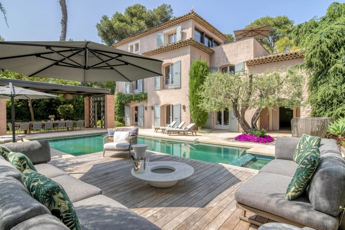 Luxurious backyard of a Mediterranean villa featuring a swimming pool, wooden deck with lounge seating, and elegant outdoor decor.
