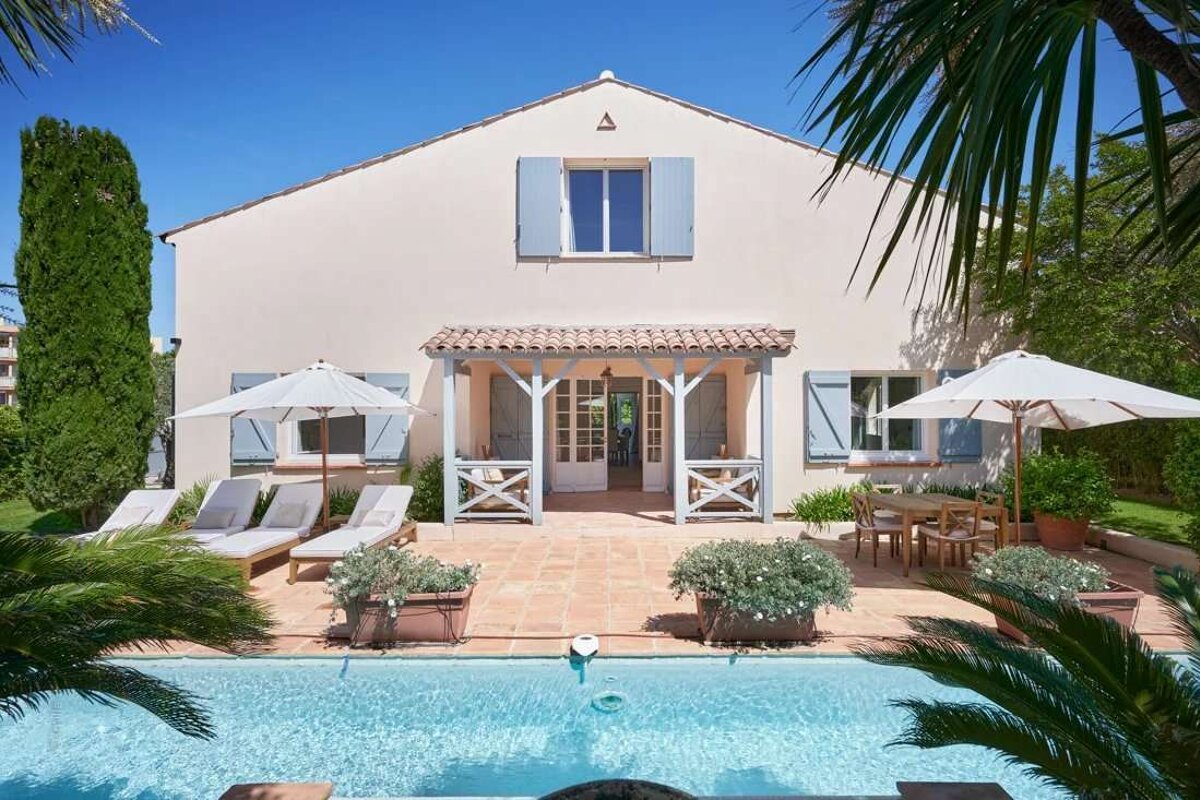 A white house with blue shutters sits next to a swimming pool