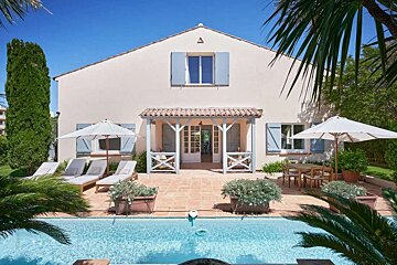 A white house with blue shutters sits next to a swimming pool