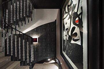 A modern staircase with unique crystal balusters, dark walls, and a large abstract painting hanging on the right.