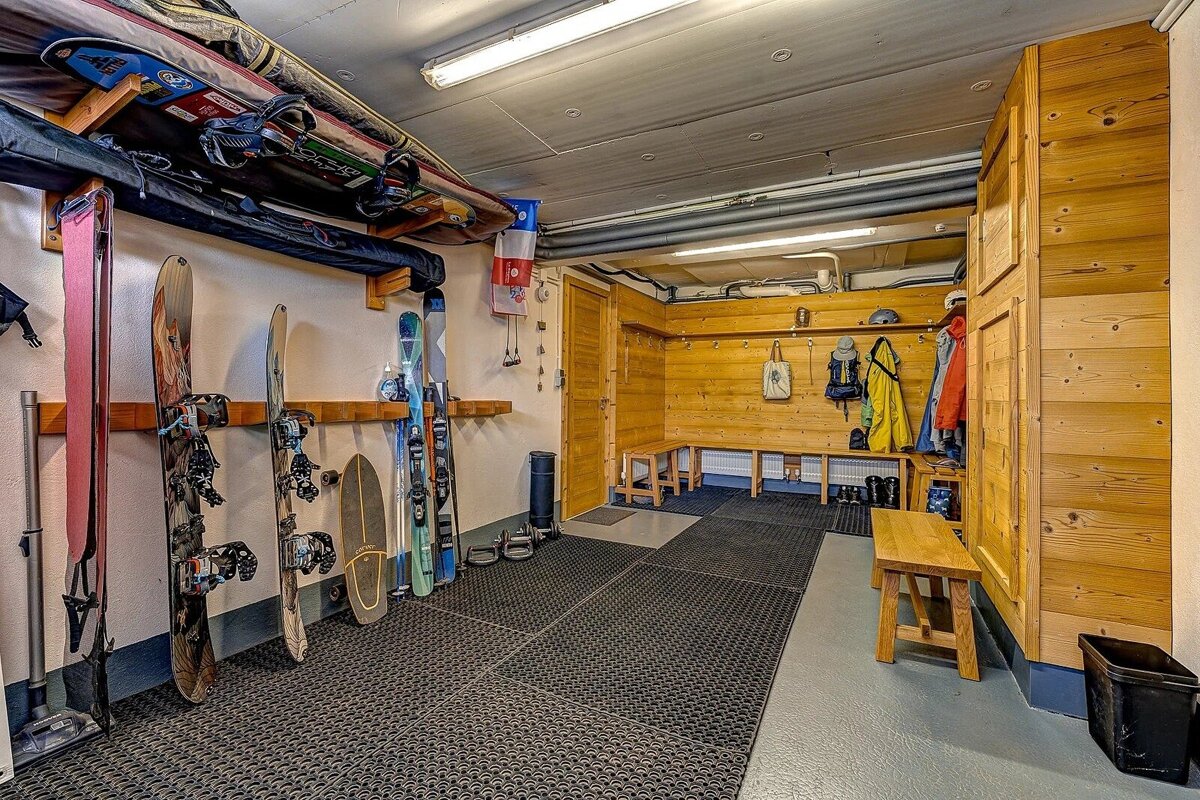 A well-organized ski/snowboard storage and changing room with wooden benches, gear racks, hooks for clothing, and protective floor mats.