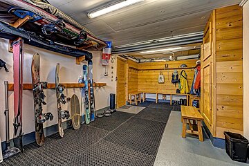A well-equipped ski locker room with skis, snowboards, bags, and outerwear stored neatly. Features wooden benches and practical floor tiling.