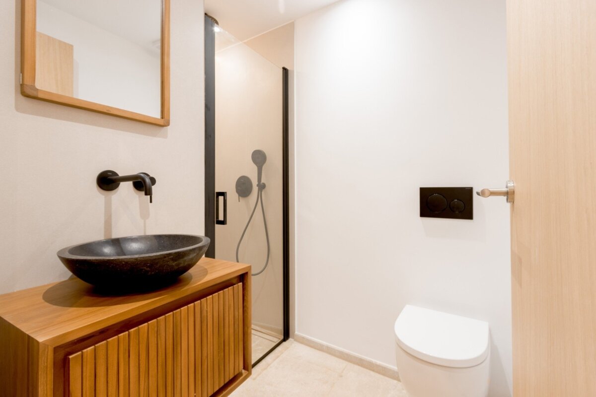 A modern bathroom featuring a black vessel sink on a wooden vanity, a walk-in glass shower, and a toilet with a black flush panel.
