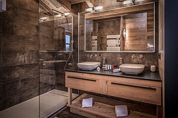 Modern rustic bathroom with a glass shower and a double wooden vanity featuring two vessel sinks under a large mirror.