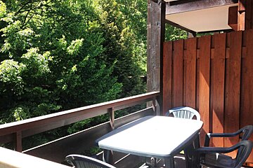 A balcony with a table and chairs and trees in the background