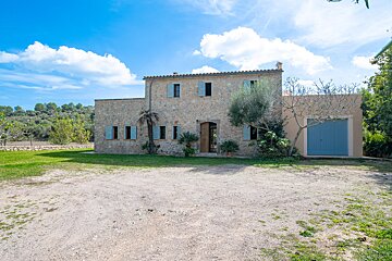 A stone house with blue shutters is surrounded by grass and trees