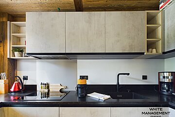 A stylish kitchen with concrete-look cabinets, black counters, and wooden details. Appliances include an induction hob, sink, and coffee maker.
