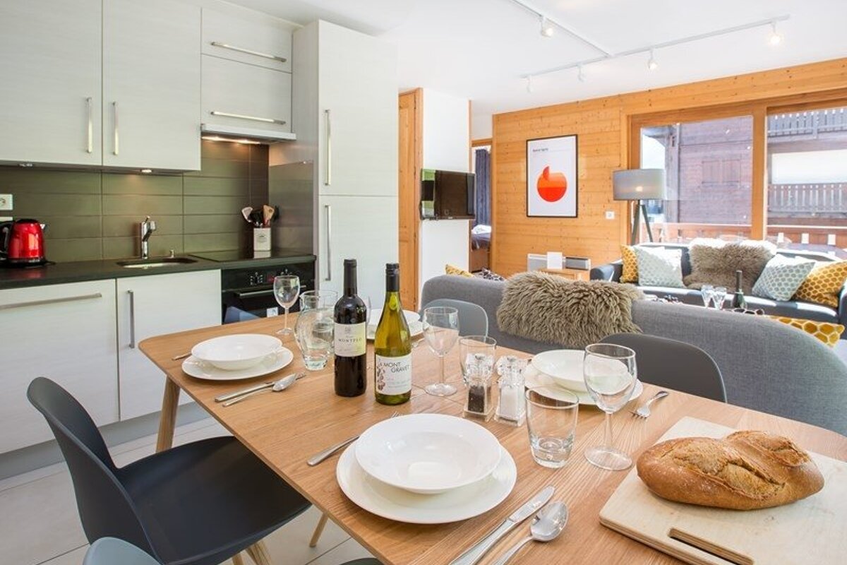Modern open-plan apartment featuring a set dining table with wine, a sleek kitchen, and a cozy living room with wooden walls.