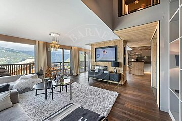 A luxurious modern living room with large windows showcasing stunning mountain views. Features include wood accents, a cozy white rug, sleek furniture, and an open-plan kitchen.