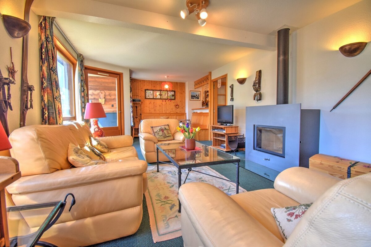 Cozy cabin-style living room with beige leather sofas, a glass coffee table, and a modern fireplace.