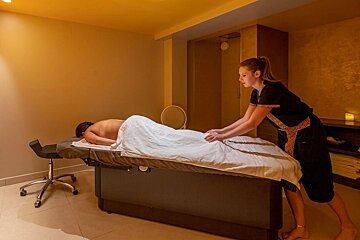 A therapist massages a client lying face down on a table in a warm-toned spa room.