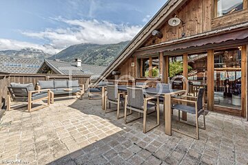 A patio with a table and chairs in front of a wooden house