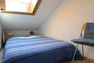 A small bedroom with a bed and a chair