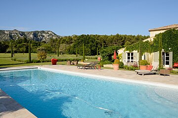 A large swimming pool in front of a house with mountains in the background