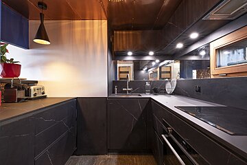 Modern, dark kitchen with black marble-effect countertops, metallic copper ceiling, sleek cabinetry, and warm integrated lighting.