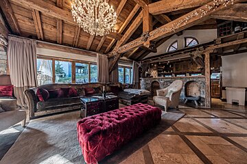 Luxurious rustic chalet living room with exposed wooden beams, a crystal chandelier, plush velvet furniture, and a stone bar area.