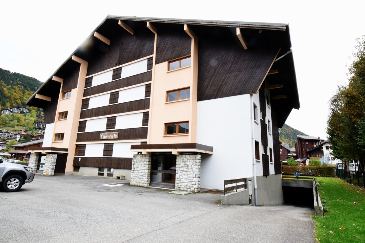 Alpine apartment building with dark wood siding, white and peach walls, and stone entryways on a paved lot.