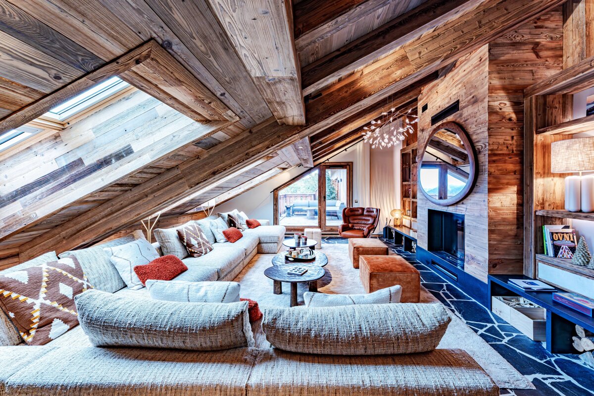 Cozy rustic chalet living room under a vaulted wooden ceiling with skylights, featuring a large sectional sofa and fireplace.