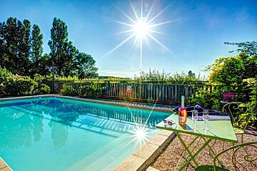 A bottle of wine sits on a table next to a swimming pool