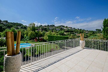 A balcony with a view of a lush green hillside and a swimming pool
