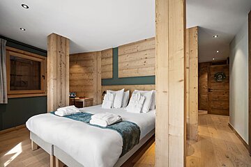 A cozy, modern alpine-style bedroom featuring light wood paneling, columns, and a bed with white linens.