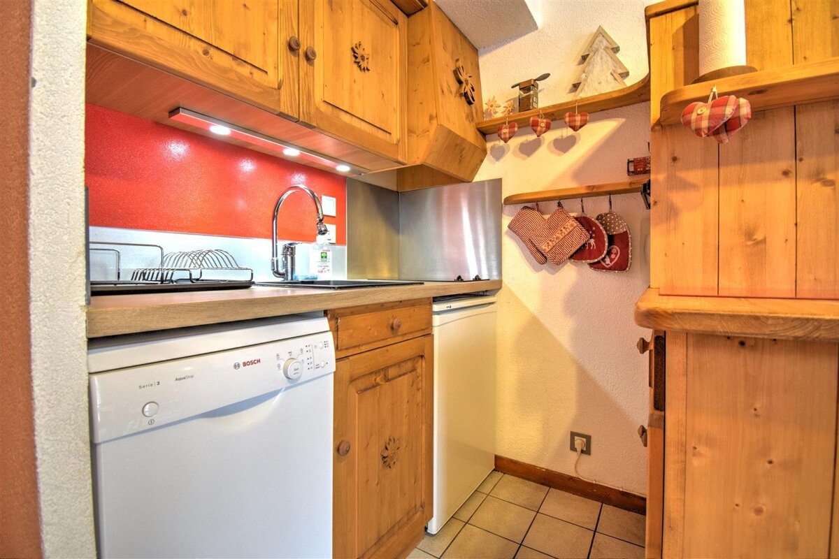 Cozy rustic kitchenette featuring light wood cabinets, a bright red backsplash, white appliances, and hanging heart decorations.
