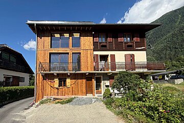 An alpine chalet with a split wood and plaster facade, featuring balconies and set against a mountain backdrop.