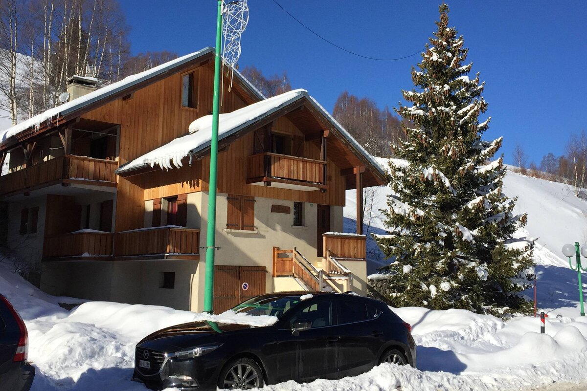 A black car is parked in front of a snowy house
