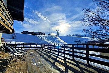 A wooden deck with chairs and a ski lift in the background