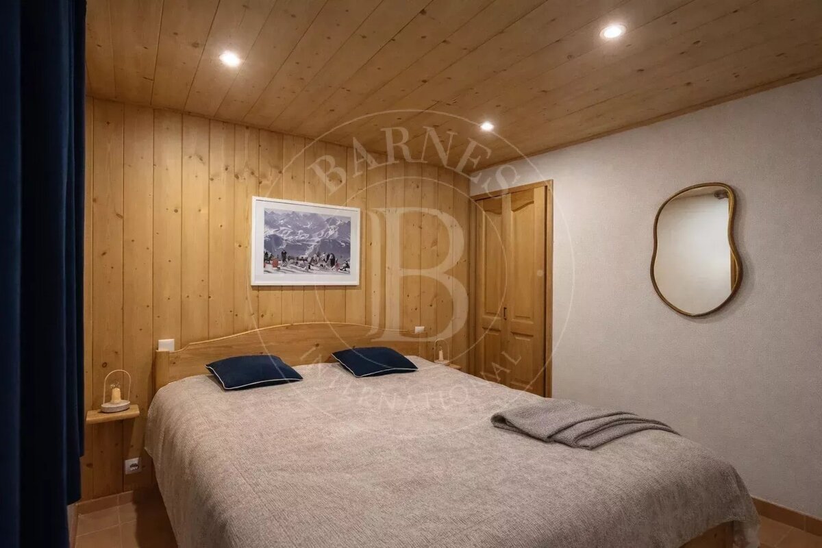 A bedroom with light wood paneling, a double bed, recessed lighting, and a mirror on the white wall.