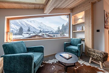 Two chairs and a table in front of a window with mountains in the background