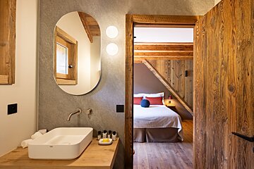 A bathroom with a sink and a mirror looking into a bedroom
