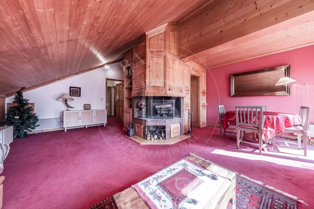 A warm room featuring a red carpet, wood ceiling, large corner fireplace, pink wall accent, dining set, and a festive Christmas tree.